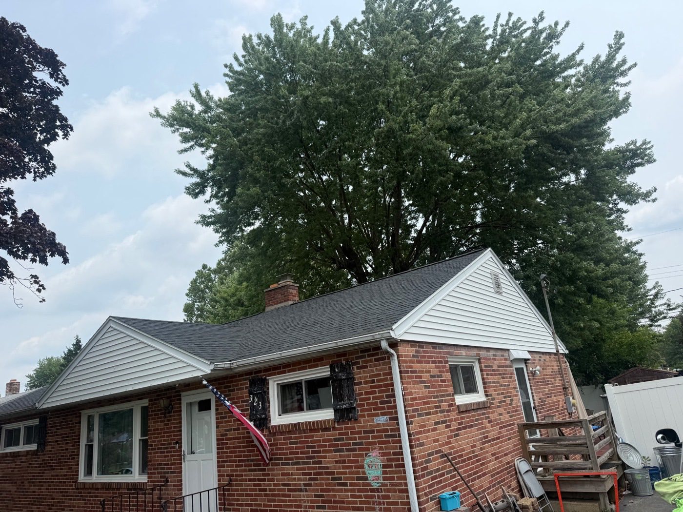 Brick Cape Cod home with white-sided gables, an American flag, and a new charcoal shingle roof
