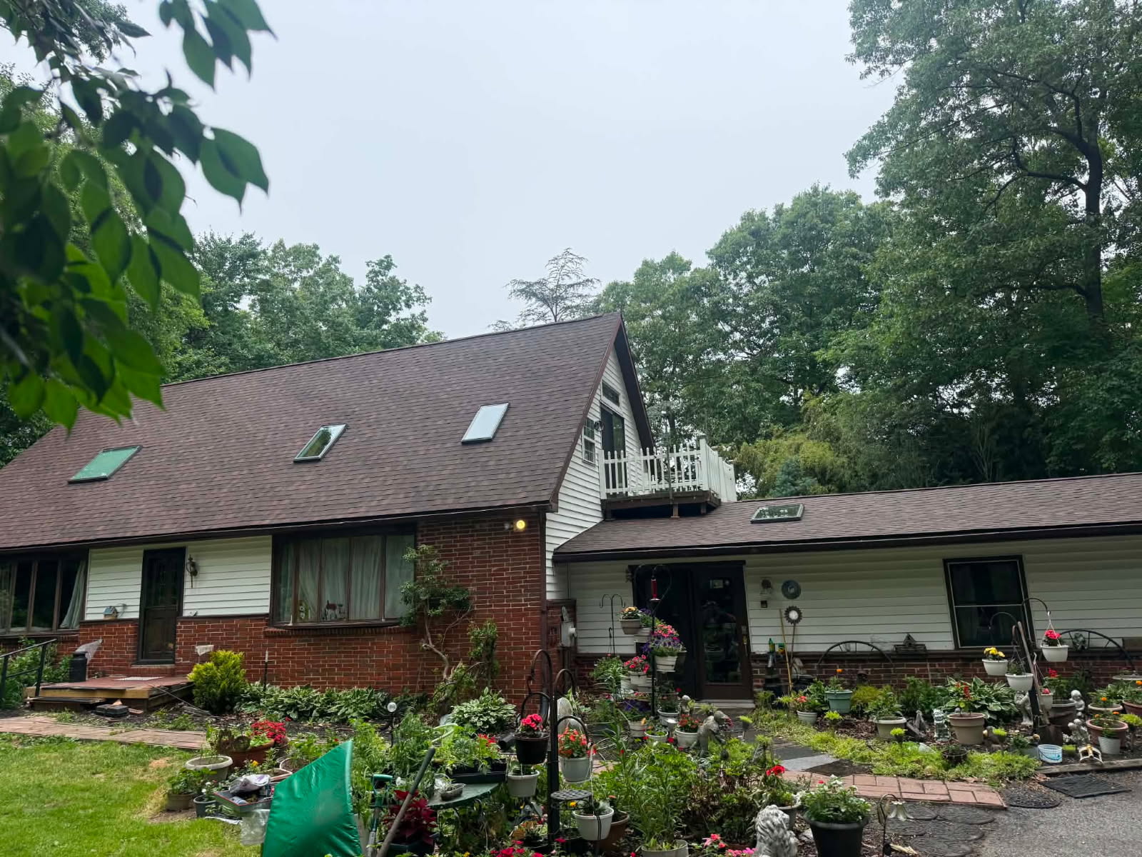 Brick and vinyl-sided cottage with a new brown architectural shingle roof and a flower garden