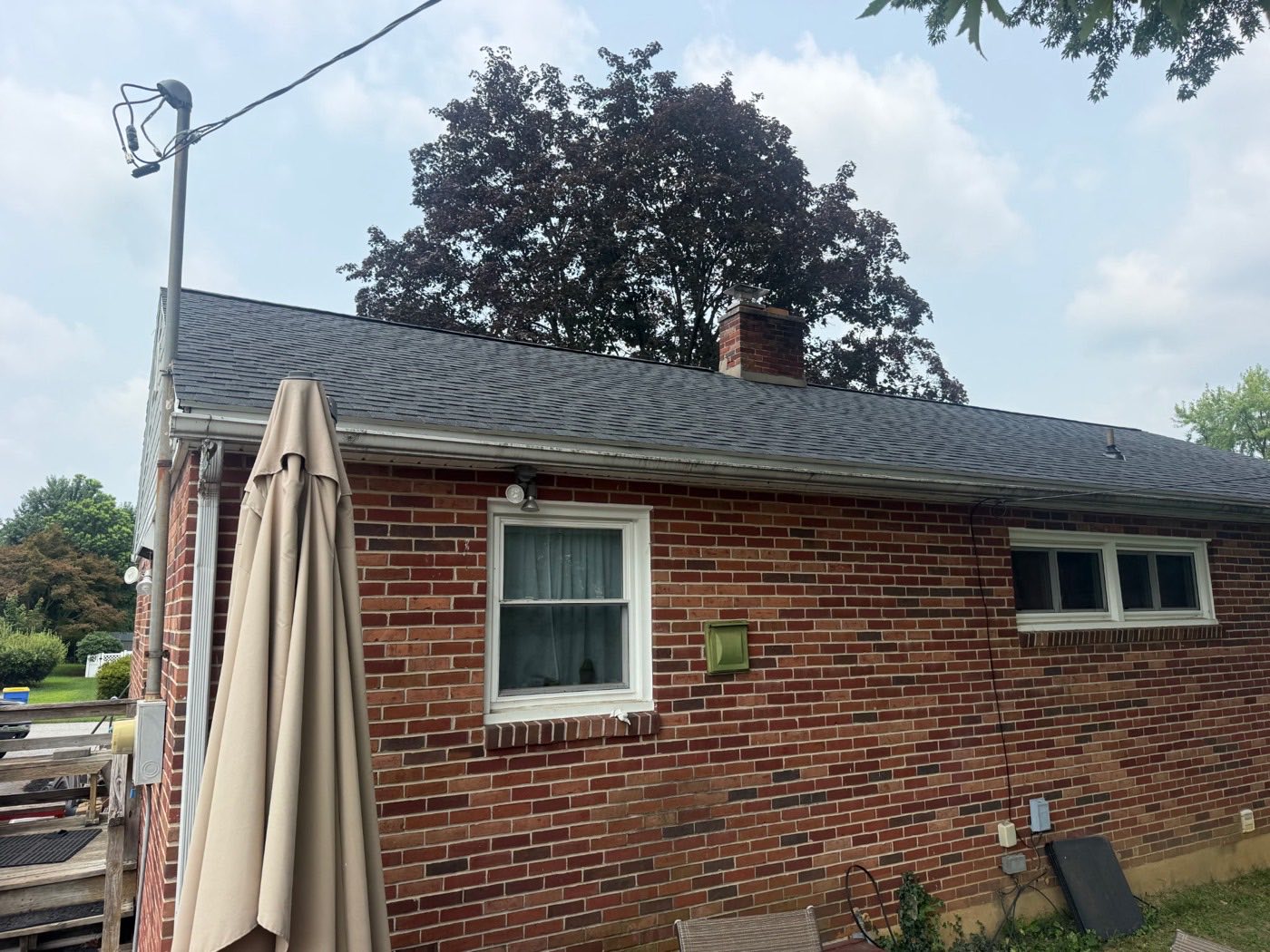 Rear of a brick ranch home with a new dark architectural shingle roof and a patio