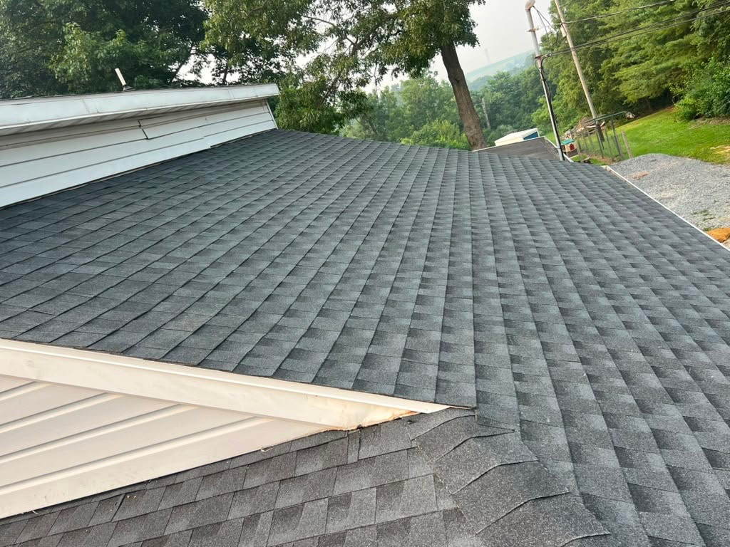 Freshly installed charcoal architectural shingle roof meeting a white-sided gable with wooded hills behind