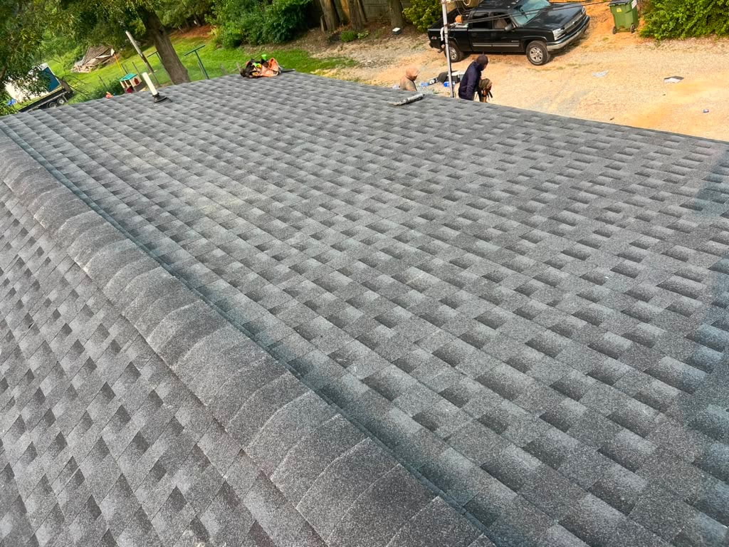 Aerial view of a newly finished charcoal architectural shingle roof with the Dallastown crew and truck staged in the gravel driveway below