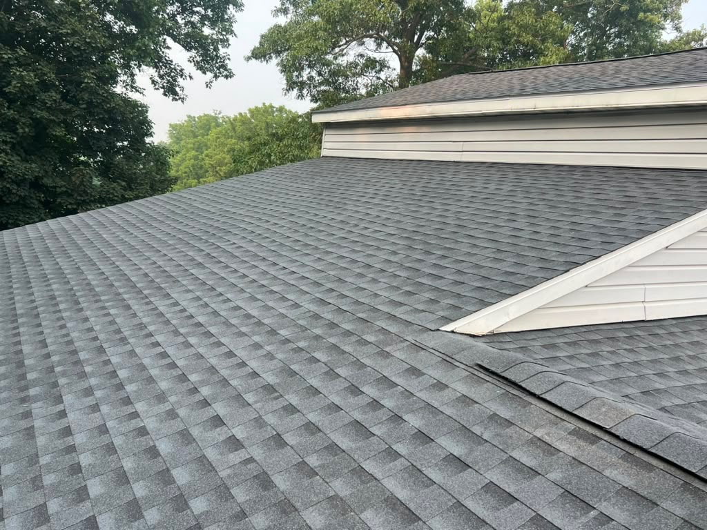 Finished charcoal architectural shingle roof with a white-sided gable surrounded by mature trees