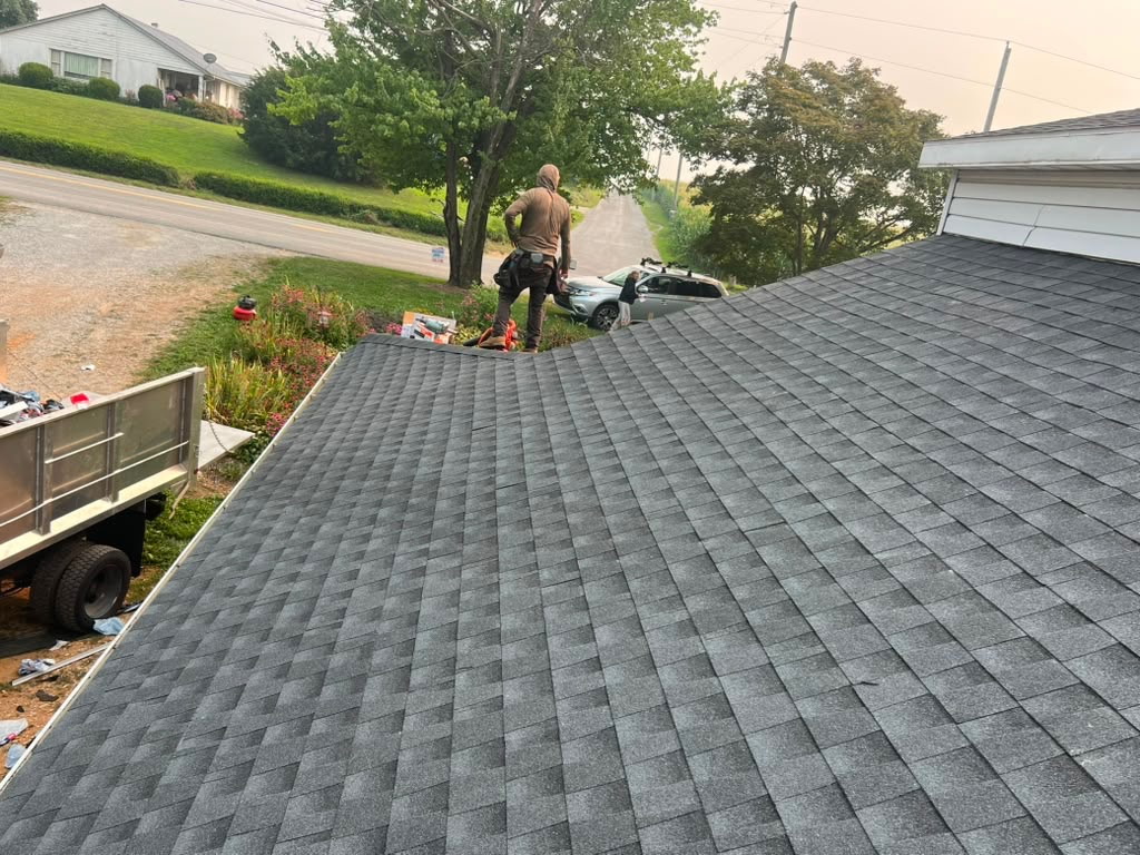 Dallastown crew member standing on a newly shingled charcoal roof overlooking a country road with the dump trailer parked below