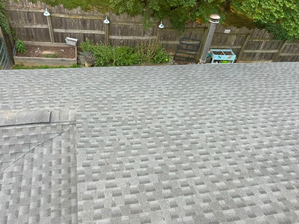 New light-grey architectural shingle hip roof above raised garden beds and a wood privacy fence