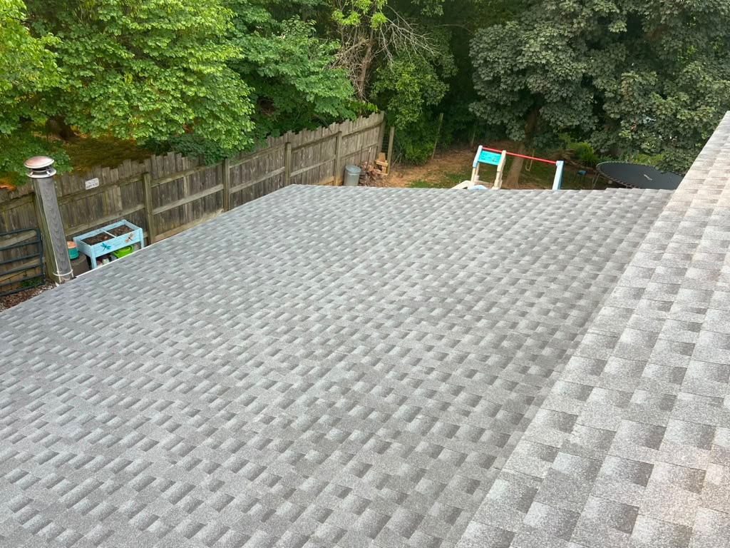 New light-grey architectural shingle roof overlooking a fenced backyard with a playset and trampoline