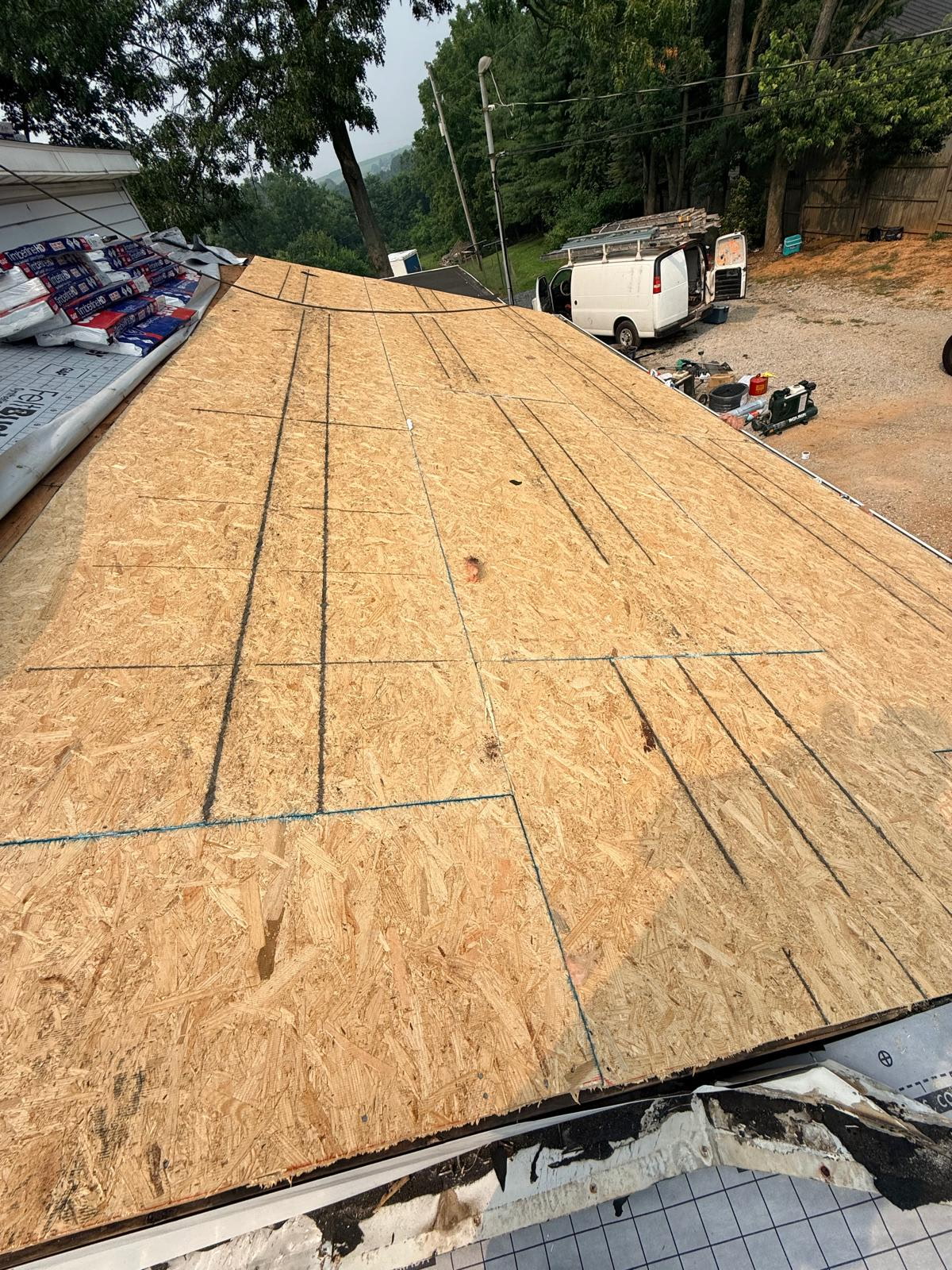 Freshly installed OSB roof decking marked with chalk lines and ready for underlayment, with the work van parked below