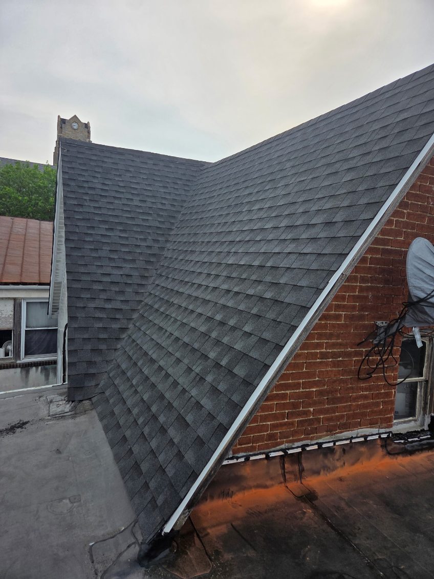 Steep grey architectural shingle roof on a brick downtown building