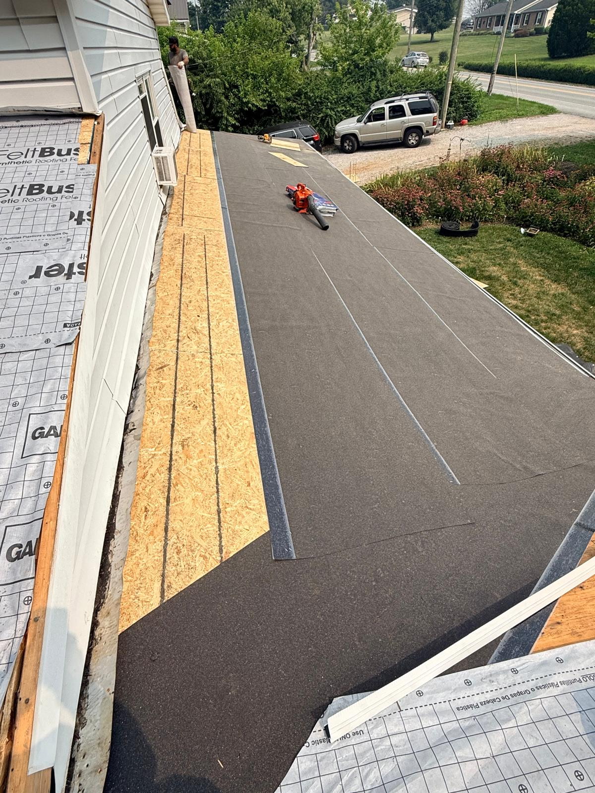 Roof re-deck in progress with new OSB sheathing and black synthetic underlayment being rolled out over a porch roof